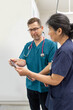 © Austockphoto - Man and woman health care workers standing next to each other looking at a tablet in the clinic