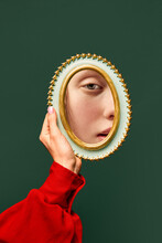 Female Hand Holding Small Mirror With Reflection Of Sad Woman's Face With Natural Make Up Over Dark Green Background. Human Emotions, Expression