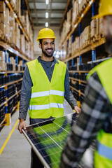 Poster - Smiling warehouse workers carring a solar panel.