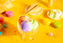 Various Colorful Ice Cream Scoops Or Balls Sundae Dish With Waffle Cones, Macaroons On Yellow Background