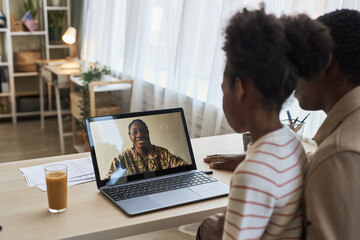Military mom having video call with her family, they sitting at table in front of laptop and talking to her