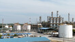A chemical or petrochemical facility, an oil refinery plant with steel pipes and chimney cooling towers, and a landscape with a blue sky in the background.