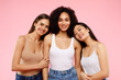 Happy multiethnic young women posing and smiling to camera, standing over pink background, studio shot