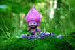 cute troll toy and amethyst minerals in forest close up, natural green background. fairytale pixie with ruffled violet hair in mystery forest. beautiful magic atmosphere. template for design