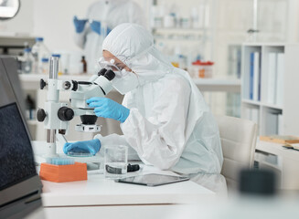 Wall Mural - its clear to see now. a scientist wearing a radiation suit while using a microscope in a lab.