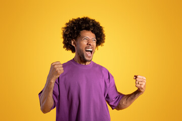 Excited excited adult african american curly man in purple t-shirt with open mouth shouting, rejoices in victory