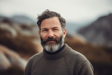 Wall Mural - Portrait of a middle-aged man with a gray beard and mustache in a warm sweater on the background of mountains