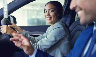 Its gonna be hard to say no.... Cropped portrait of an attractive young woman sitting in a new car while speaking to a handsome male car salesman about a deal.