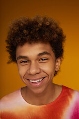 Wall Mural - Face of cute smiling teenage boy in trendy t-shirt looking at you while standing in front of camera against yellow background in studio