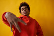 © Seventyfour - Youthful African American guy in red hoodie looking at camera while standing on yellow background and keeping right hand in front of him