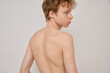 Portrait of handsome male with red curly hair standing with naked back and arms with freckles on grey background. Man without clothes on a neutral background. Male beauty concept.