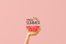 Hand With Piece Of Ripe Watermelon And Text HELLO, SUMMER On Pink Background