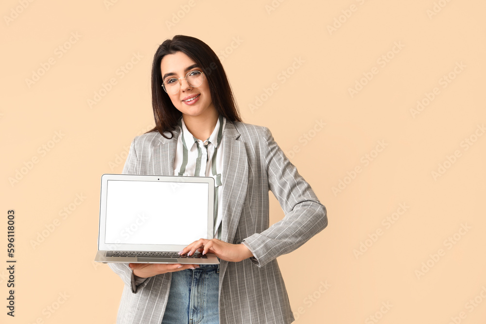 Young female programmer with laptop on beige background