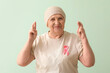 © Pixel-Shot - Senior woman after chemotherapy with pink ribbon crossing fingers on green background. Breast cancer concept