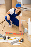 Fototapeta  - Smiling young woman professional builder laying laminate flooring in repairable room ..
