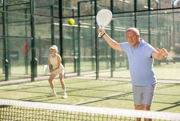 Wall Mural - Motivated senior man playing padel with his teammate in court