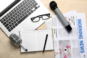 Laptop with eyeglasses, microphones, notebook and newspapers on light wooden background