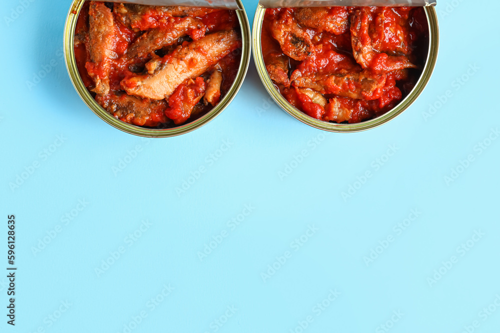 Opened tin cans with fish in tomato sauce on blue background