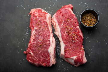 Close up of raw strip loin steaks on black cutting board with salt and spices.