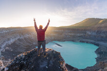 Victorious Mountaineer Man In Front Of Poas Volcano Crater Lagoon At Sunrise Surrounded By Volcanic Rocks In Poas Volcano National Park In Alajuela Province Of Costa Rica