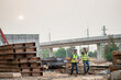 A team of civil engineers and architects wearing safety gear inspect the construction site of a high concrete bridge at a highway construction site.