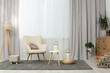 © New Africa - Comfortable armchair, white table and stylish lanterns near elegant curtains in light room. Interior design