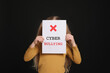 © New Africa - Girl holding sign with phrase Cyber Bullying on black background