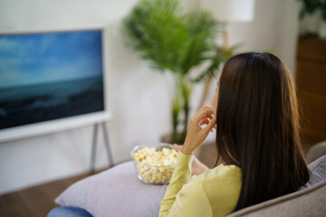 Wall Mural - Asian woman Watching smart TV and using remote controller Hand holding television audio remote control at home with the remote control television