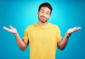 Wall Mural - Confused, question and portrait of man shoulder shrugging and raise arms isolated in a blue studio background. Clueless, smile and young male person with doubt, whatever and doing a hand gesture