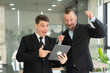 © ArLawKa - Two young businessmen looking at laptop smiling and expressing joy that the business succeeded according to their plans colleague talking to each other describing good partnership