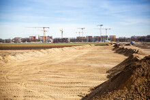 Germany, Bavaria, Munich, Sandy Area Prepared For Construction Site With Industrial Cranes In Background