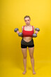 © Ivan Zelenin - Beautiful model in sportswear with dumbbells looks at the camera on yellow, red and dark background
