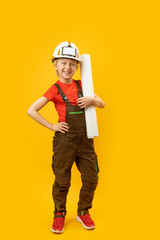 Wall Mural - Smiling boy in protective helmet, overalls and with roll of paper in his hands. Child as builder or architect. Vertical frame.