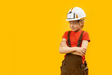 Poster - Smiling boy in protective helmet, glasses and jumpsuit like worker. Yellow background. Copy space, mock up