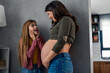 © Dorde - Young cheerful girl looking at her happy smiling pregnant mother with excitement while standing together at home.