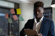 © JustLife - Portrait of successful businessman in office. Young African man witing ideas on colorful stickers on glass wall..