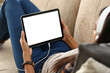 © H_Ko - Mockup image of a digital tablet with black screen in hands of woman in headphones. Person resting at home on sofa with tablet over shoulder view