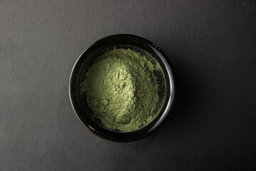 Wall Mural - Green powder in a small ceramic bowl,  on a black background.  Super food or marijuana kief concept