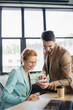 © LIGHTFIELD STUDIOS - smiling bearded businessman showing smartphone to woman in eyeglasses in office.