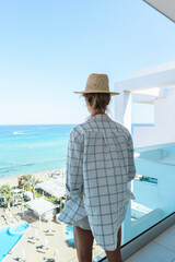 Wall Mural - Woman wearing straw hat enjoy view from balcony of beachfront hotel or apartment