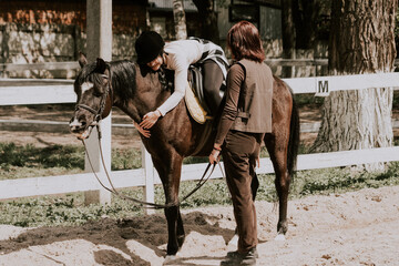 A woman instructor teaching girl how to ride a horse.  Female rider practicing on a horseback learning equestrian sport. Active lifestyle and leisure activity concep