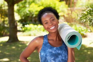 Wall Mural - Portrait of a Black woman standing ready for yoga in park, rolled up mat