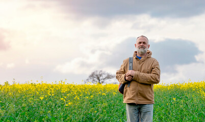 Bearded happy pensioner with a backpack in the rapeseed field.  Travel  Lifestyle concept