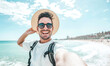 © Davide Angelini - Happy man with hat and sunglasses taking selfie picture with smartphone at the beach