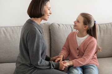 Wall Mural - Positive european millennial mother holding hand, talk with teenage girl, enjoy communication in living room