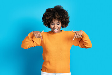 Wall Mural - Excited pretty young black woman pointing down, blue background