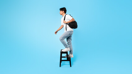 Wall Mural - Asian Teenager Boy Walking Up Stairs Holding Backpack, Blue Background