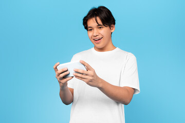 Wall Mural - Chinese Guy Using Phone Playing Game Online On Blue Background