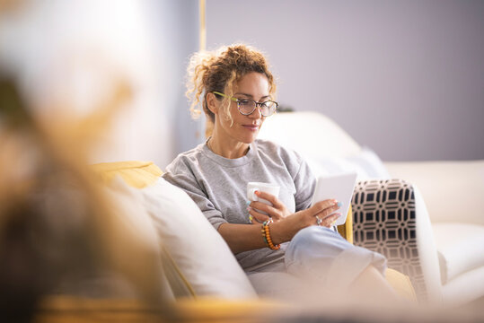 Modern lady having relax at home sitting on couch and using ereader tablet to read an online ebook. Woman using technology indoor leisure activity alone enjoying relaxation on couch. Indoor life
