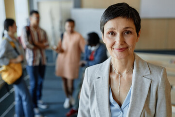 Wall Mural - Portrait of professional lecturer looking at camera while standing in lecture hall with group of students in background